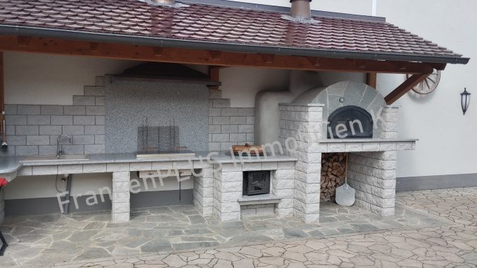 Gartenkamin mit Grillfläche und Holzofen, umgeben von einem gepflasterten Boden.