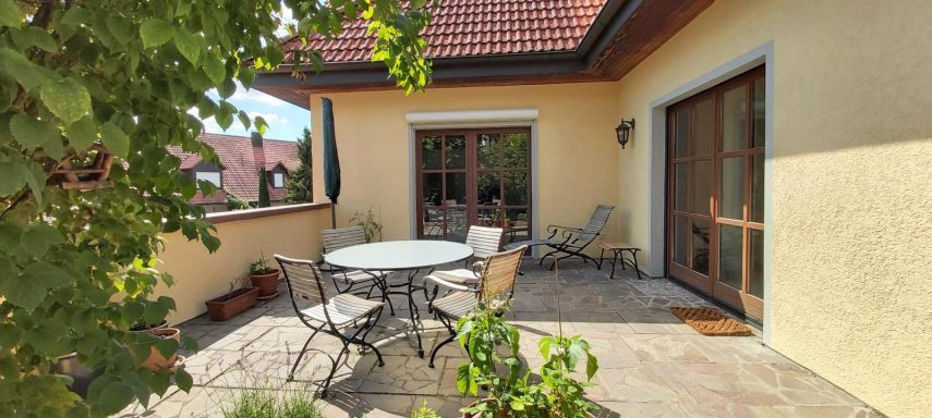 Gemütliche Terrasse mit Tisch, Stühlen und Pflanzen im sonnigen Außenbereich.