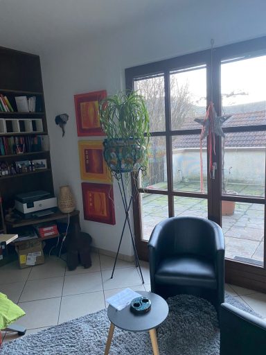 Gemütliche Ecke mit schwarzem Sessel, Tisch, Topfpflanze und Fensterblick nach außen.