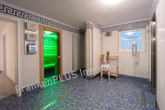 Saunabereich mit grüner Beleuchtung, Stuhl und Duschbereich. Elegant gefliest.